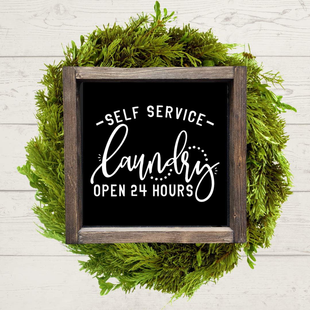 Dark brown stained 9x9 framed laundry room sign with a black background and white lettering that says self service laundry, open 24 hours.