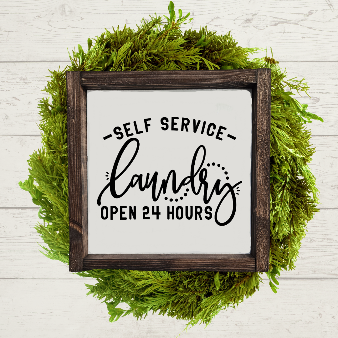 Dark brown stained 9x9 framed laundry room sign with a white background and black lettering that says self service laundry, open 24 hours.