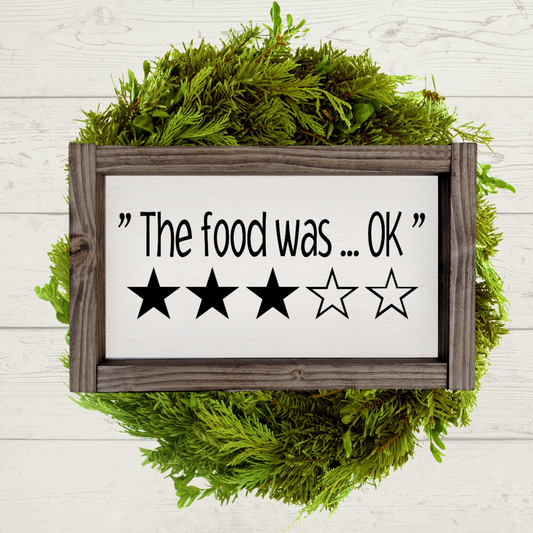 5x9 inch wooden kitchen sign that says the food was ok with a 3 star rating painted in black and white with a brown farmhouse frame.